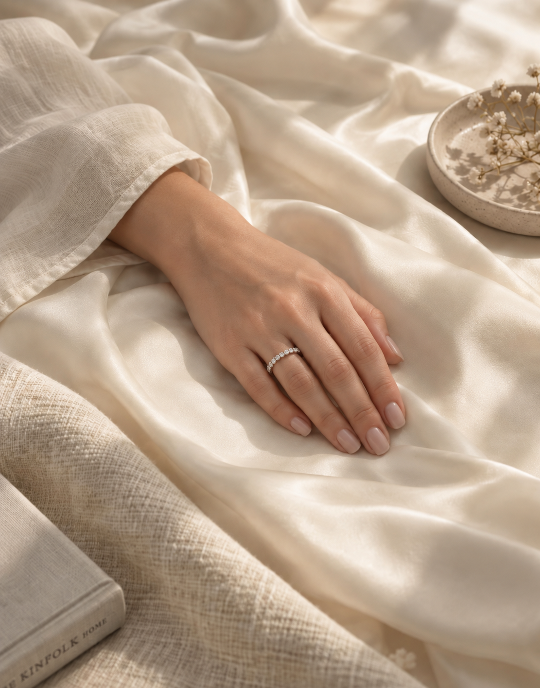 A hand wearing a delicate half-eternity moissanite band against a warm ivory background
