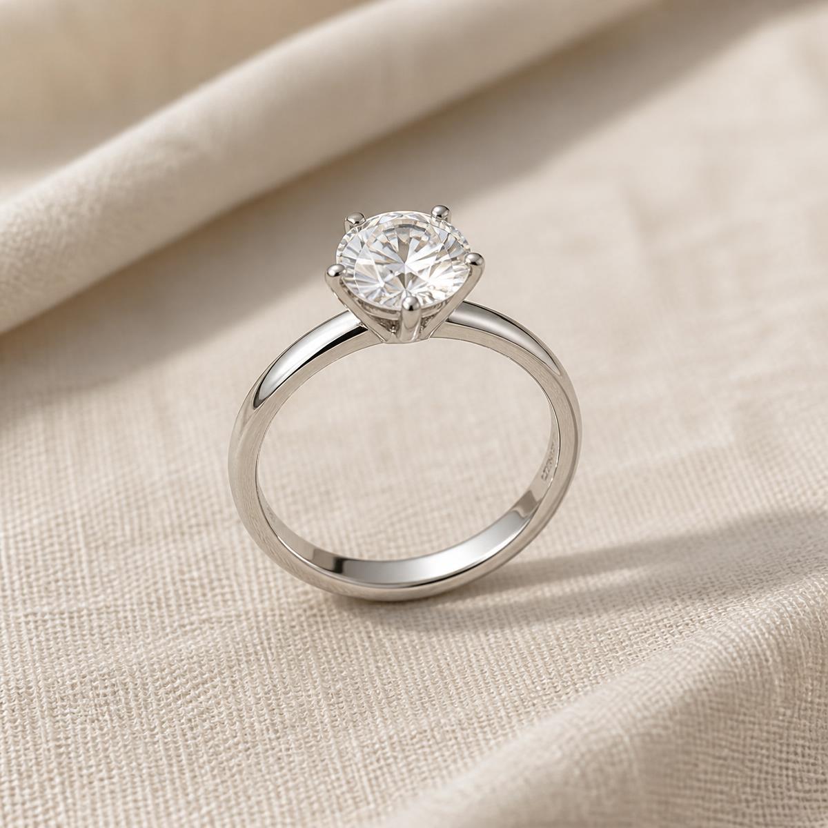 Round solitaire moissanite ring with a white-gold finish on ivory linen