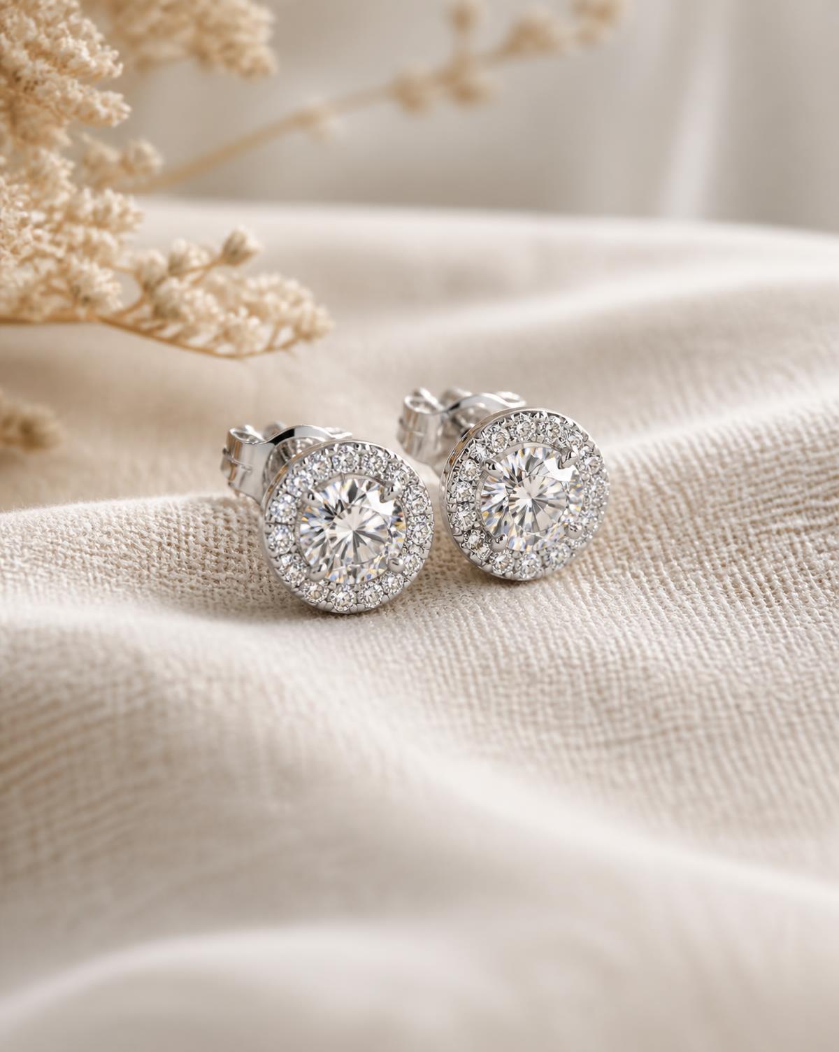Pair of halo moissanite stud earrings with a white-gold finish on ivory linen