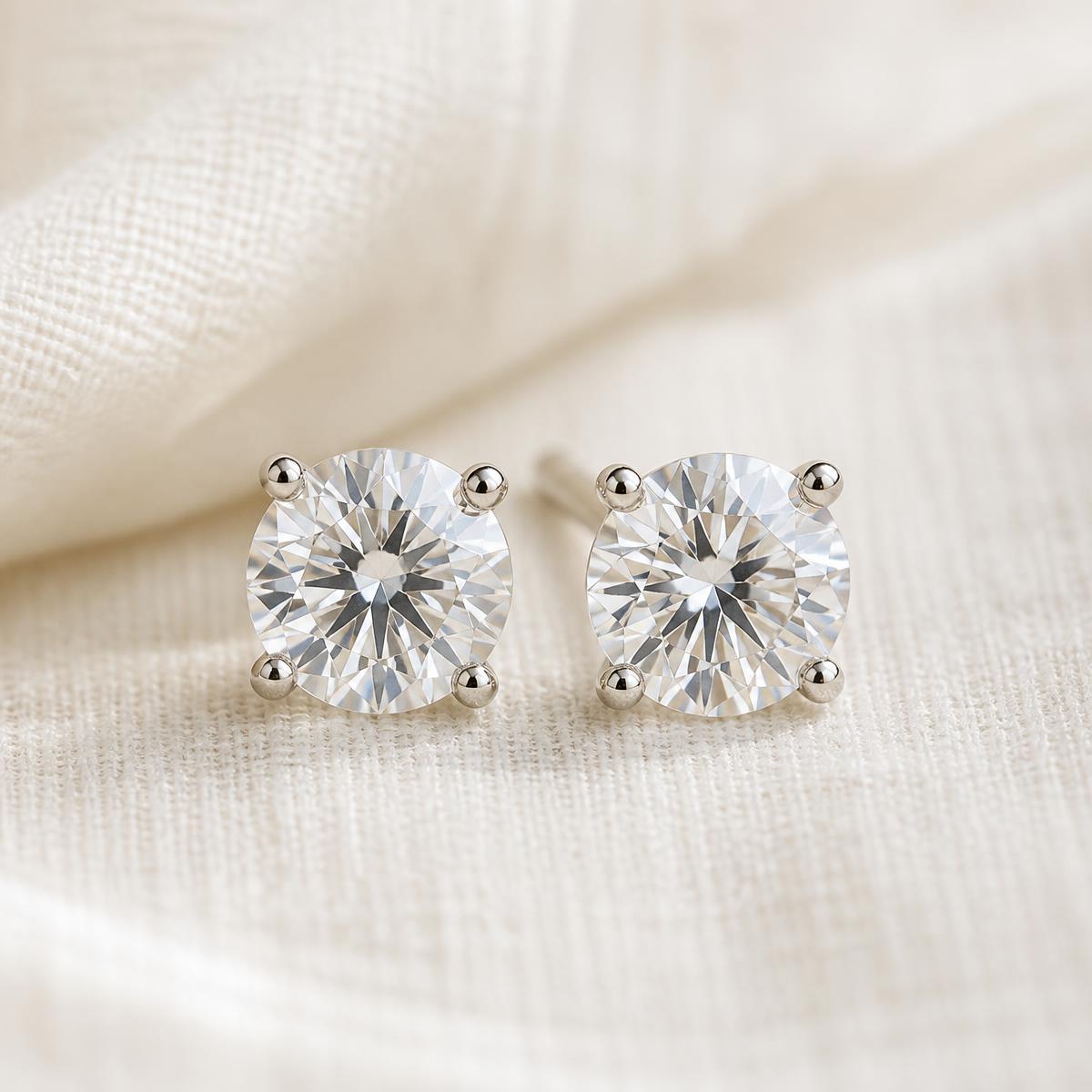 Pair of round moissanite stud earrings with a white-gold finish on ivory linen