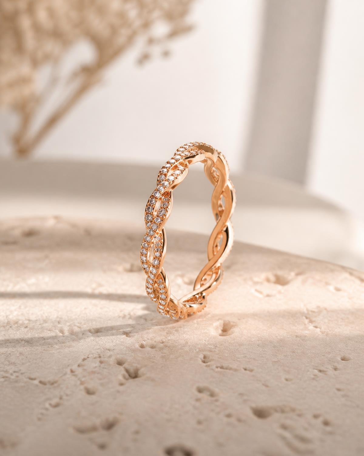 Twisted eternity band in rose-gold finish set with small moissanite stones, standing on warm stone