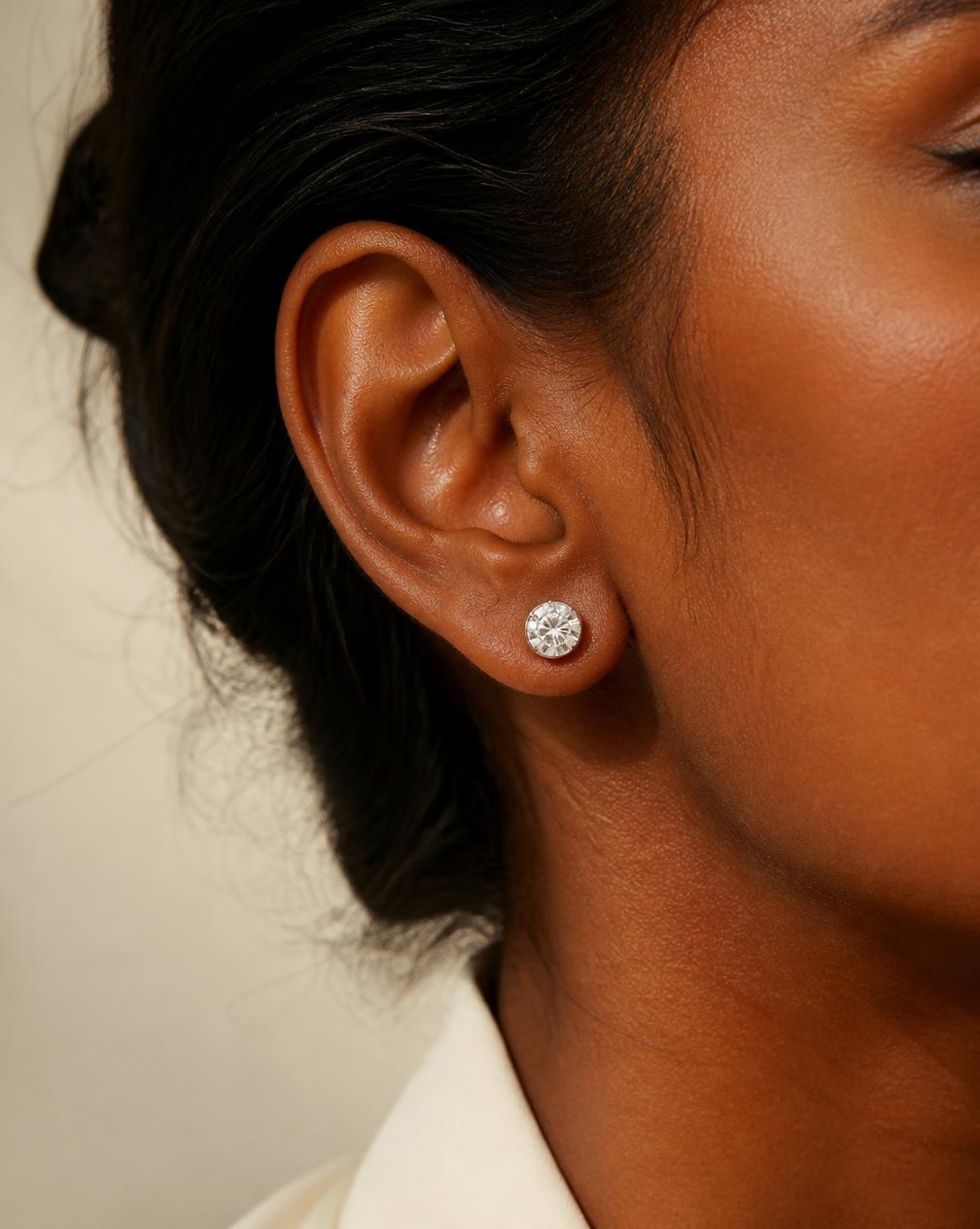 A round moissanite stud earring worn on an ear in natural light
