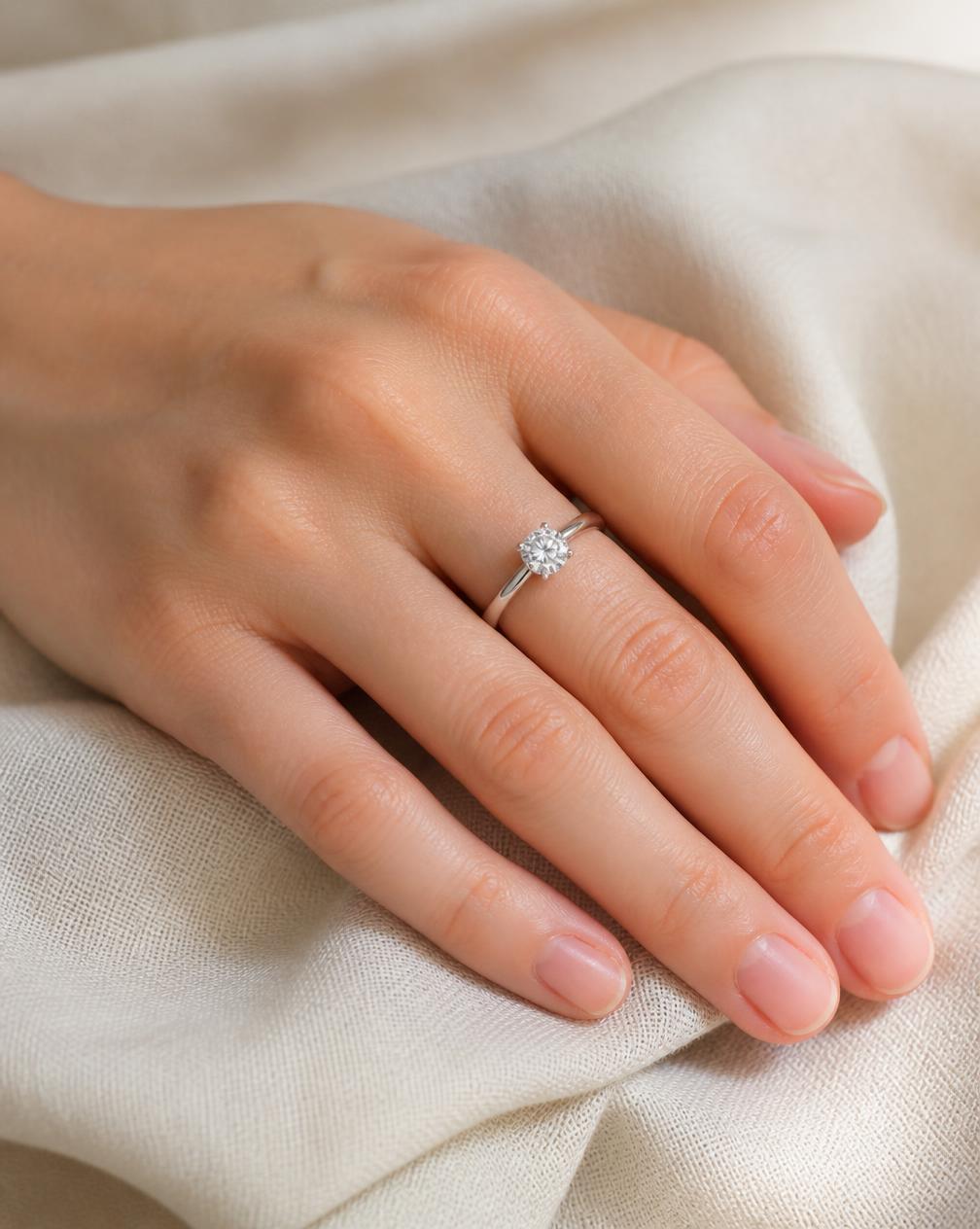 A solitaire moissanite ring worn on a hand resting on linen